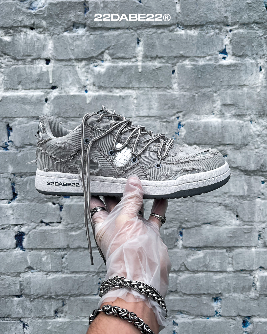 The DABE RANGER TWENTYTWO GREY shoe, a streetwear statement piece with metallic details under denim fabric on the upper. The shoe features double laces for extra style and versatility. Each shoe is handmade and unique, with every hole made by hand, giving it a one-of-a-kind look. The shoe is perfect for those who want to stand out from the crowd and make a fashion statement.