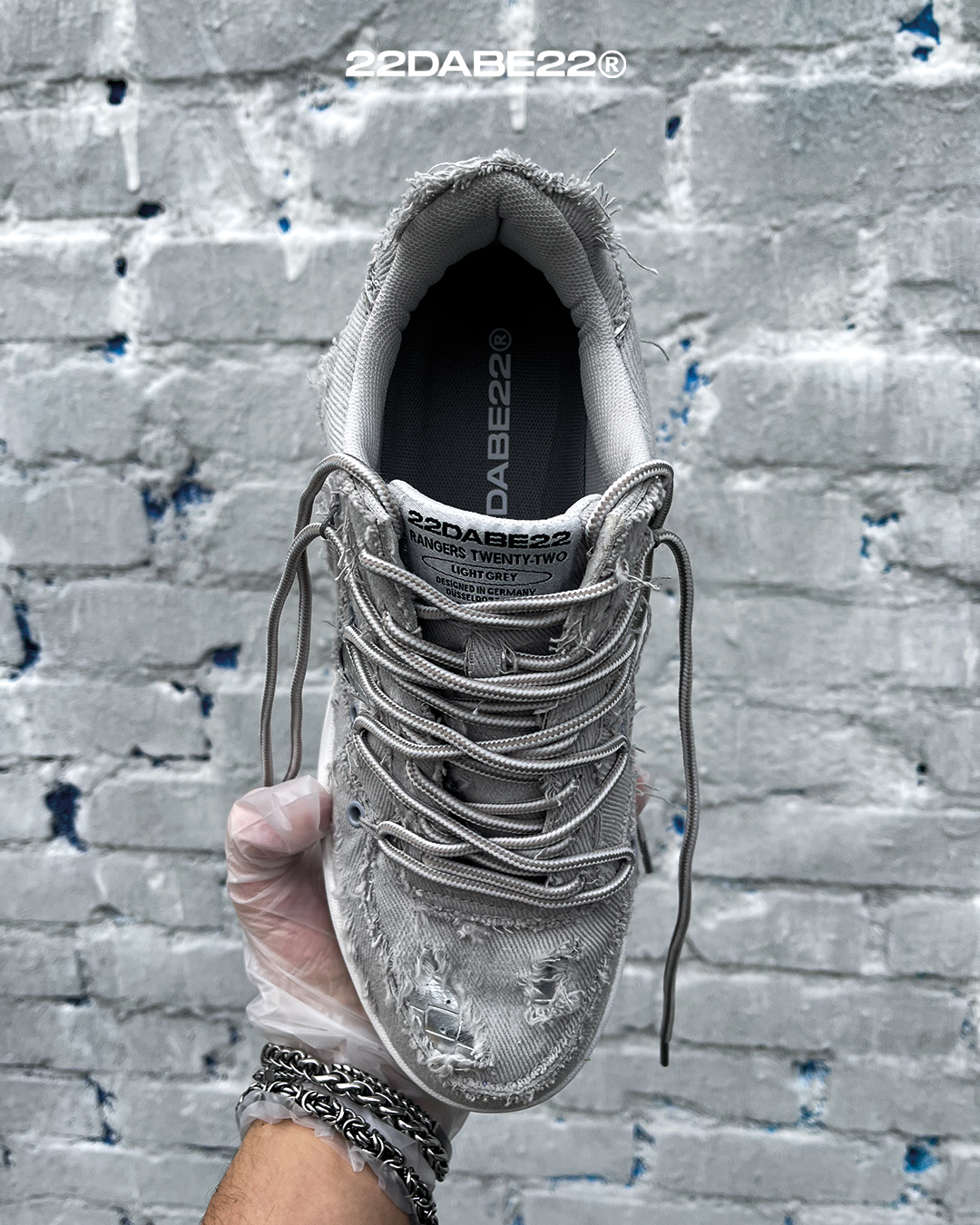 The DABE RANGER TWENTYTWO GREY shoe, a streetwear statement piece with metallic details under denim fabric on the upper. The shoe features double laces for extra style and versatility. Each shoe is handmade and unique, with every hole made by hand, giving it a one-of-a-kind look. The shoe is perfect for those who want to stand out from the crowd and make a fashion statement.