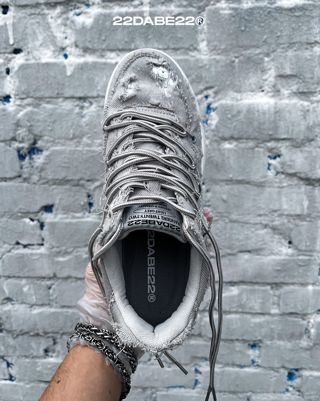 The DABE RANGER TWENTYTWO GREY shoe, a streetwear statement piece with metallic details under denim fabric on the upper. The shoe features double laces for extra style and versatility. Each shoe is handmade and unique, with every hole made by hand, giving it a one-of-a-kind look. The shoe is perfect for those who want to stand out from the crowd and make a fashion statement.