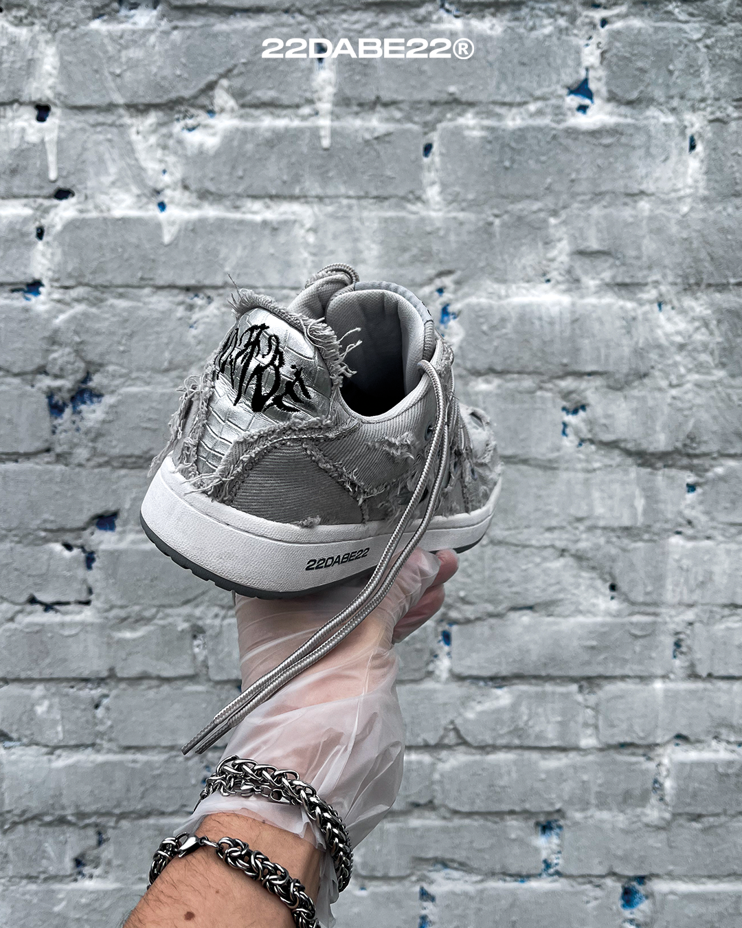 The DABE RANGER TWENTYTWO GREY shoe, a streetwear statement piece with metallic details under denim fabric on the upper. The shoe features double laces for extra style and versatility. Each shoe is handmade and unique, with every hole made by hand, giving it a one-of-a-kind look. The shoe is perfect for those who want to stand out from the crowd and make a fashion statement.