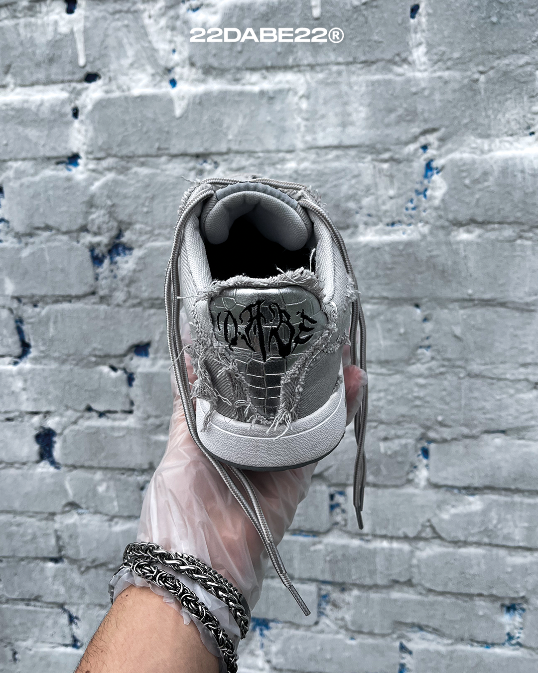 The DABE RANGER TWENTYTWO GREY shoe, a streetwear statement piece with metallic details under denim fabric on the upper. The shoe features double laces for extra style and versatility. Each shoe is handmade and unique, with every hole made by hand, giving it a one-of-a-kind look. The shoe is perfect for those who want to stand out from the crowd and make a fashion statement.
