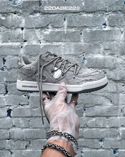 The DABE RANGER TWENTYTWO GREY shoe, a streetwear statement piece with metallic details under denim fabric on the upper. The shoe features double laces for extra style and versatility. Each shoe is handmade and unique, with every hole made by hand, giving it a one-of-a-kind look. The shoe is perfect for those who want to stand out from the crowd and make a fashion statement.