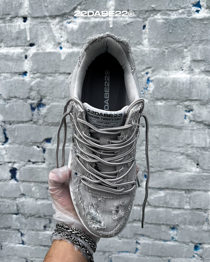 The DABE RANGER TWENTYTWO GREY shoe, a streetwear statement piece with metallic details under denim fabric on the upper. The shoe features double laces for extra style and versatility. Each shoe is handmade and unique, with every hole made by hand, giving it a one-of-a-kind look. The shoe is perfect for those who want to stand out from the crowd and make a fashion statement.
