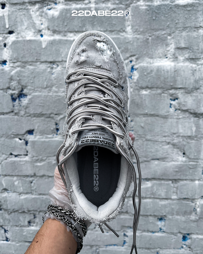 The DABE RANGER TWENTYTWO GREY shoe, a streetwear statement piece with metallic details under denim fabric on the upper. The shoe features double laces for extra style and versatility. Each shoe is handmade and unique, with every hole made by hand, giving it a one-of-a-kind look. The shoe is perfect for those who want to stand out from the crowd and make a fashion statement.