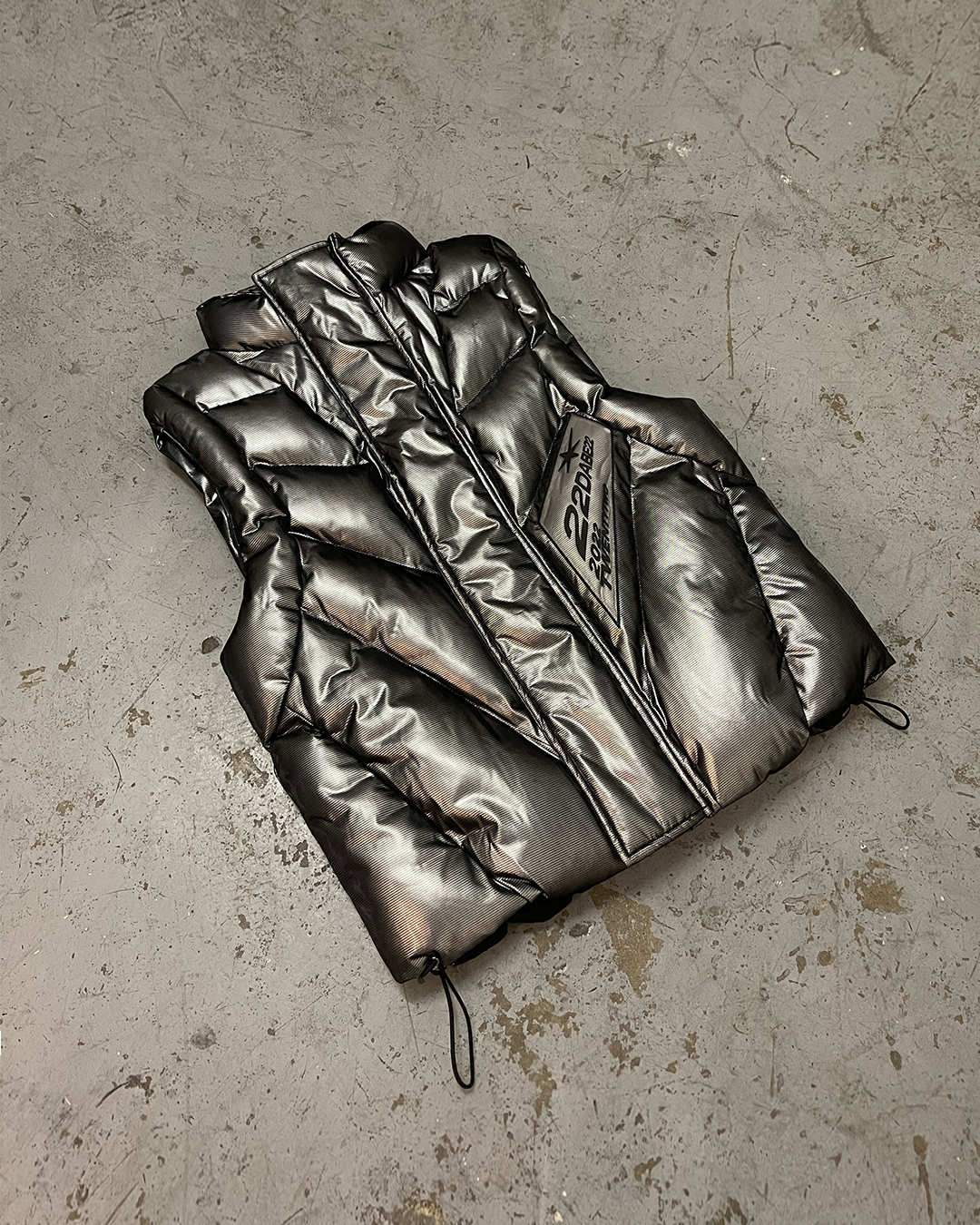 Metallic Dark Grey Vest by 22DABE22. Puffed vest made from a special manufactured fabric for warmth and comfort. Features transparent silicone patch and two front pockets. Oversized fit for layering. Made from 73% Polyester and 27% PU Leather. Perfect for braving chilly weather in style.