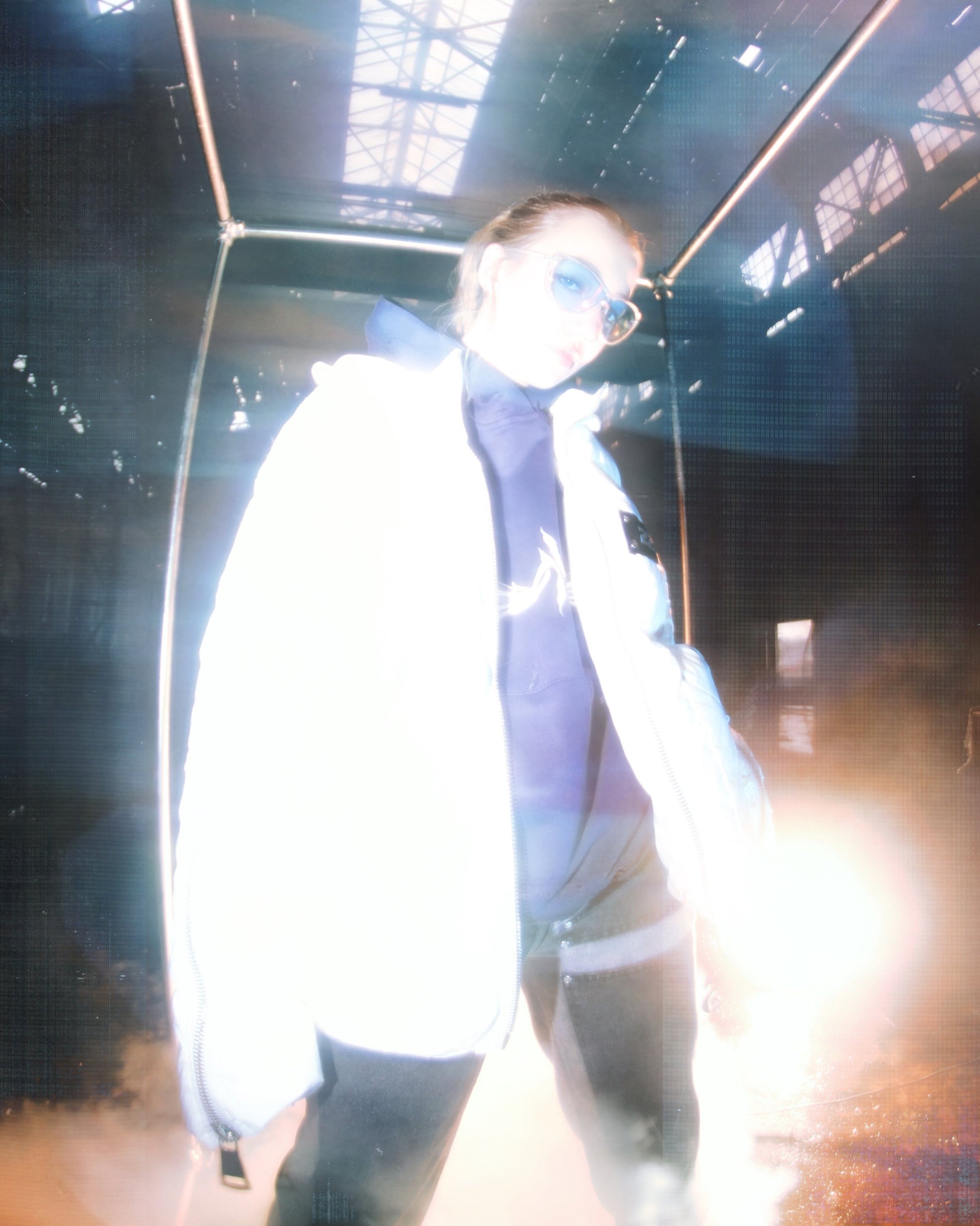A white puffer jacket from 22DABE22, made of high-quality nylon fabric and cotton down filling, featuring custom logo rivets and buttons, detachable hood, and adjustable drawcords on the bottom hem. The jacket has an oversized fit, with sleeves that can be unzipped for unrestricted movement and ample storage space with one inside pocket and two side pockets. The logo tape at the chest adds a touch of branding.